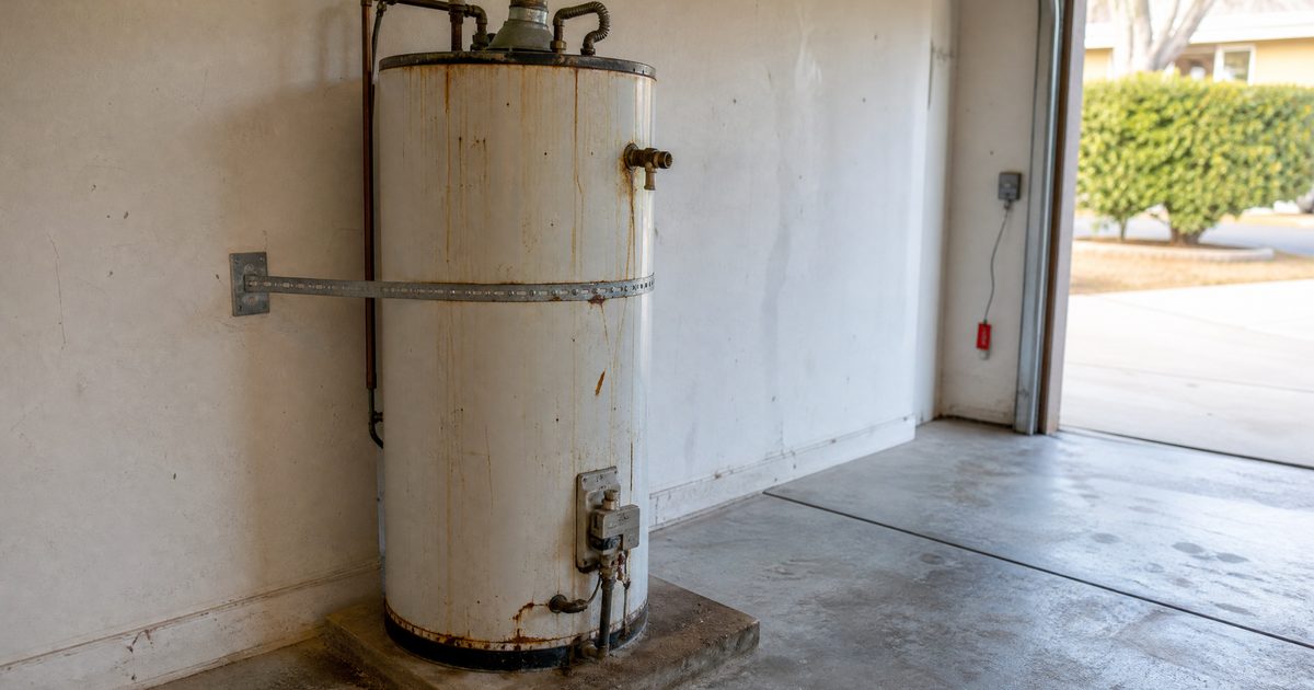 Aging tank water heater with rust staining and corroded fittings in a Hollister home garage